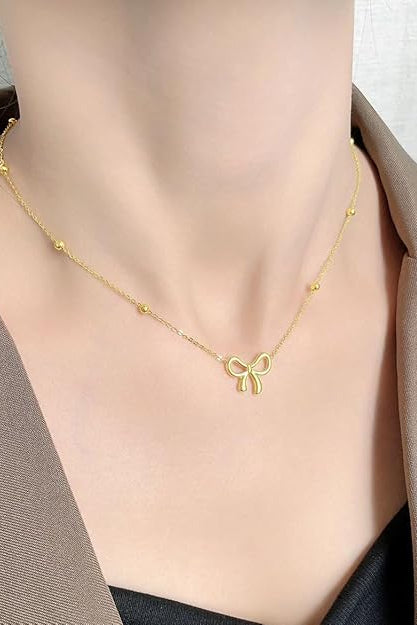 Gold-tone bow charm necklace worn as a delicate everyday necklace